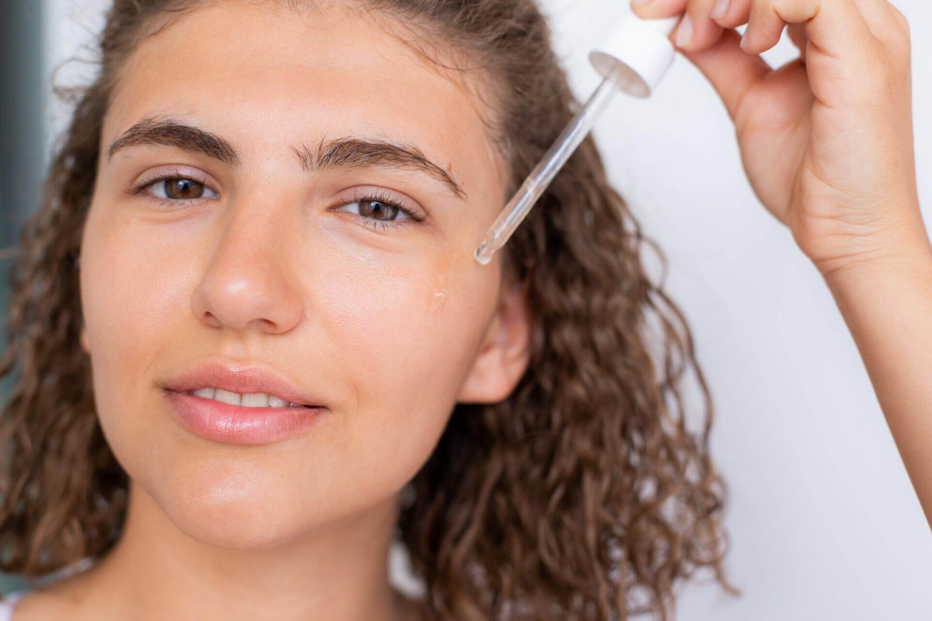 young curly haired woman using serum for her face 2023 11 27 05 06 20 utc