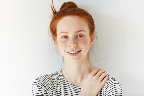 isolated headshot of pretty teenager with perfect clean skin with freckles, wearing striped top, looking and smiling at the camera with happy and joyful expression. people and lifestyle concept