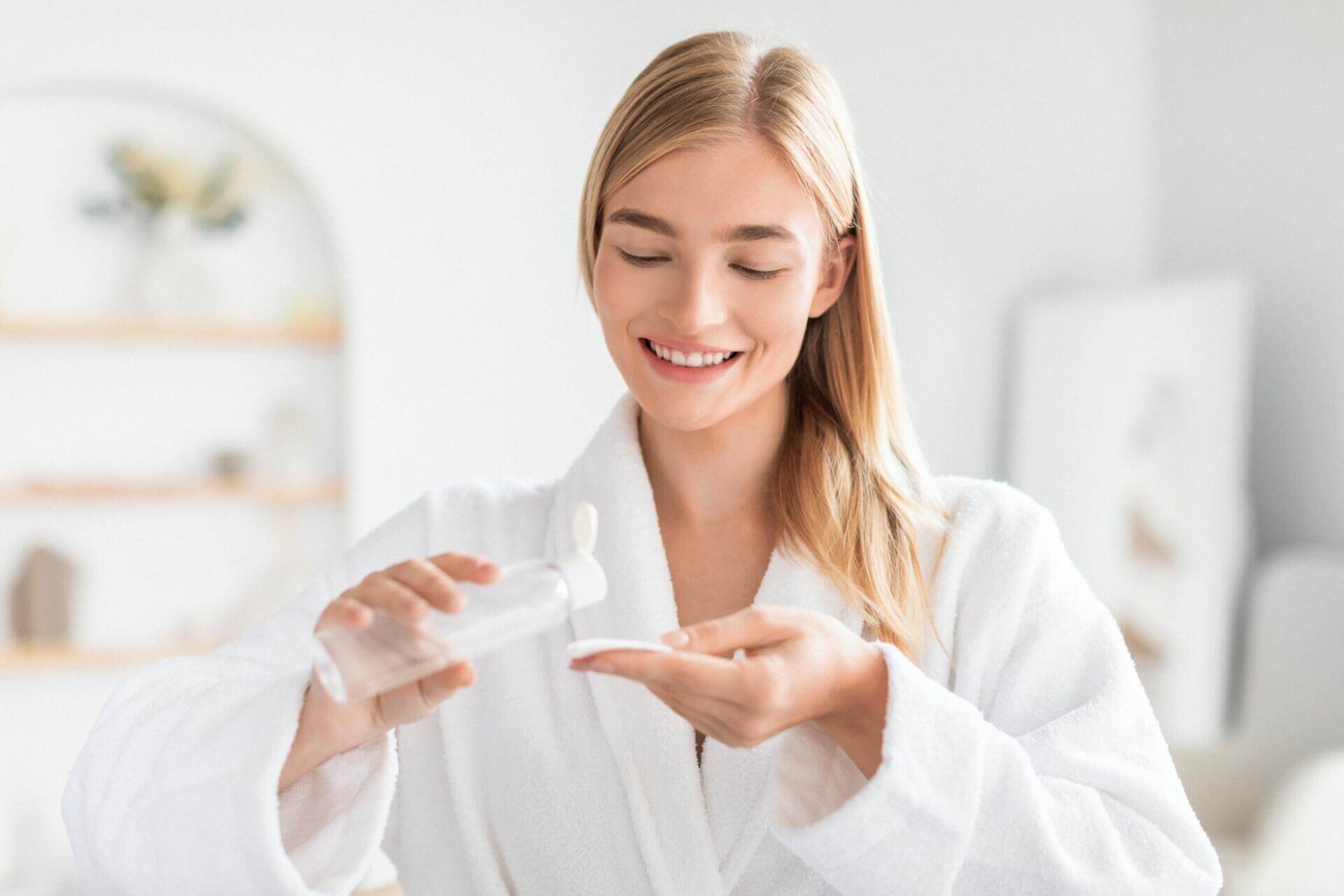 blonde woman applies micellar water on cotton pad in bathroom