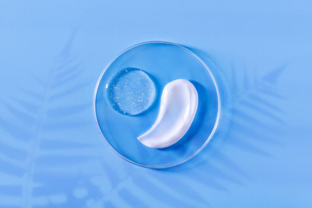 smear of cream round transparent drop of transparent gel serum in a petri dish on a blue background