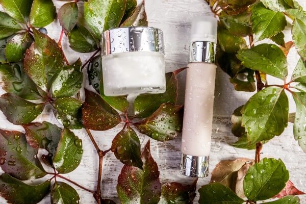 spa cosmetic bottle products on white wooden background and green leaves covered in fresh water drops