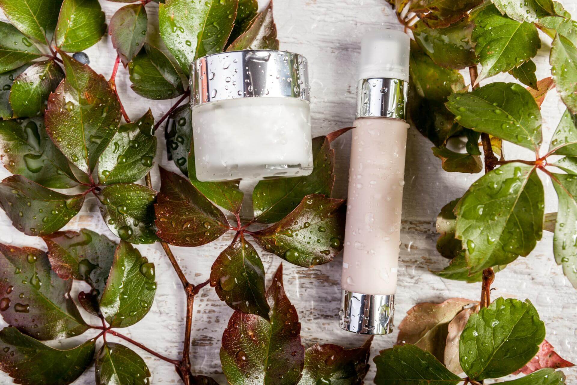 spa cosmetic bottle products on white wooden background and green leaves covered in fresh water drops