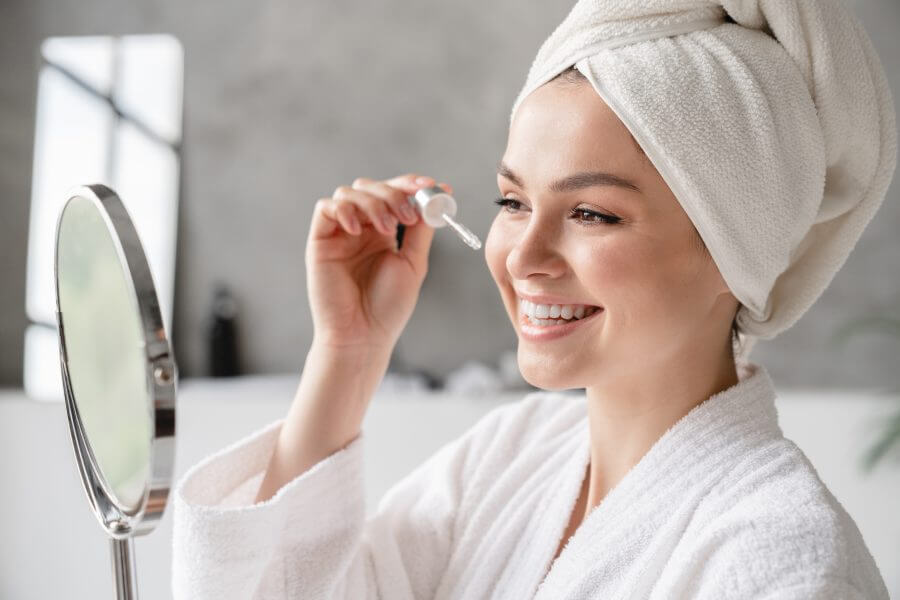 young white woman in bath spa towel applying rejuvenation moisturizing serum on her face