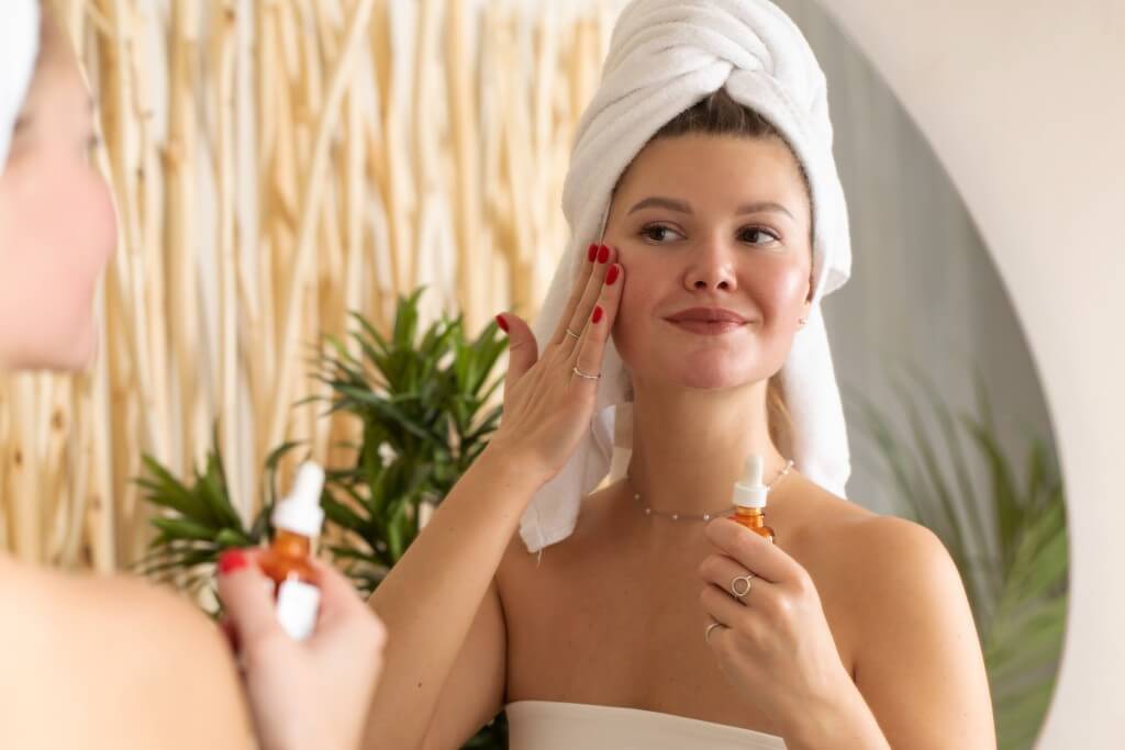 an attractive woman in front of a mirror applies a serum to the skin of the face in the bathroom.