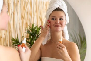 an attractive woman in front of a mirror applies a serum to the skin of the face in the bathroom.