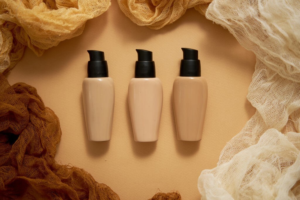 bottles of three different shades of makeup foundation on beige