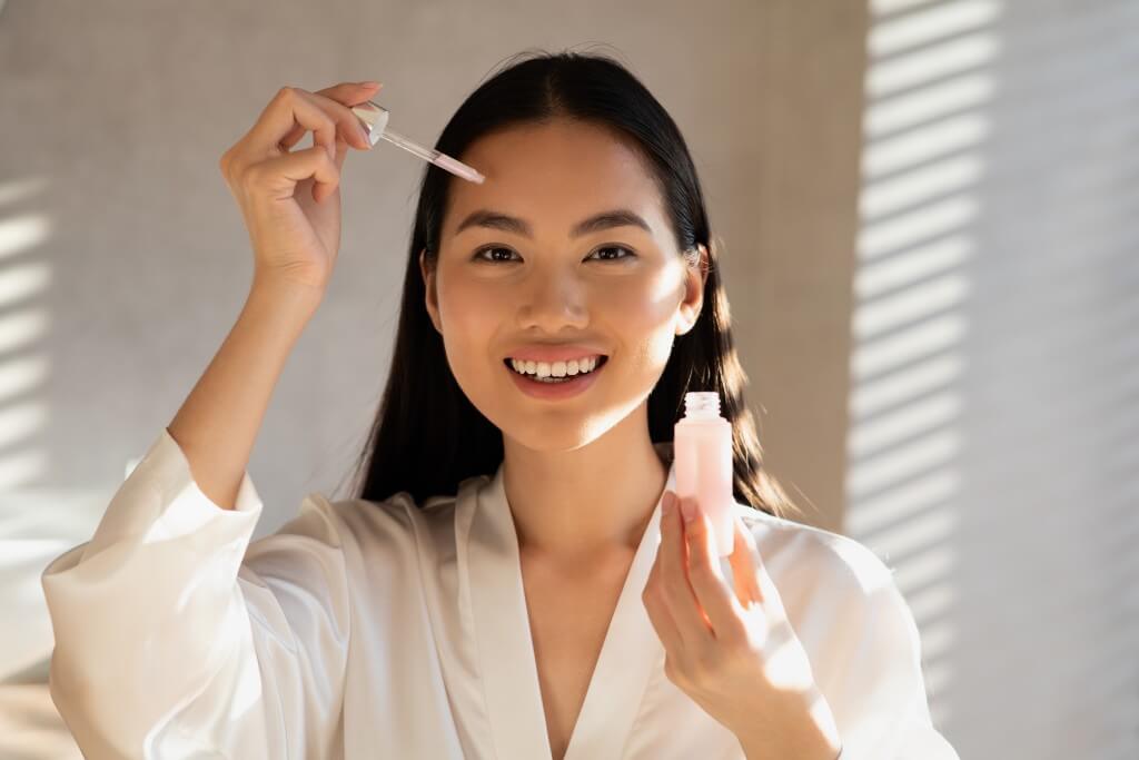 cheerful pretty chinese woman applying beauty product on forehead