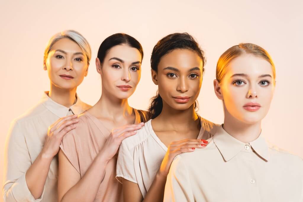 four beautiful multicultural women looking at camera isolated on beige