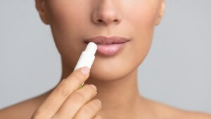 girl applying hygienic lip balm on grey background