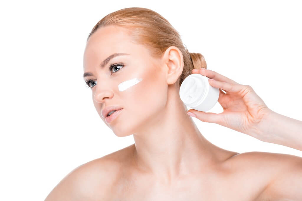 portrait of woman showing face cream and looking away isolated on white