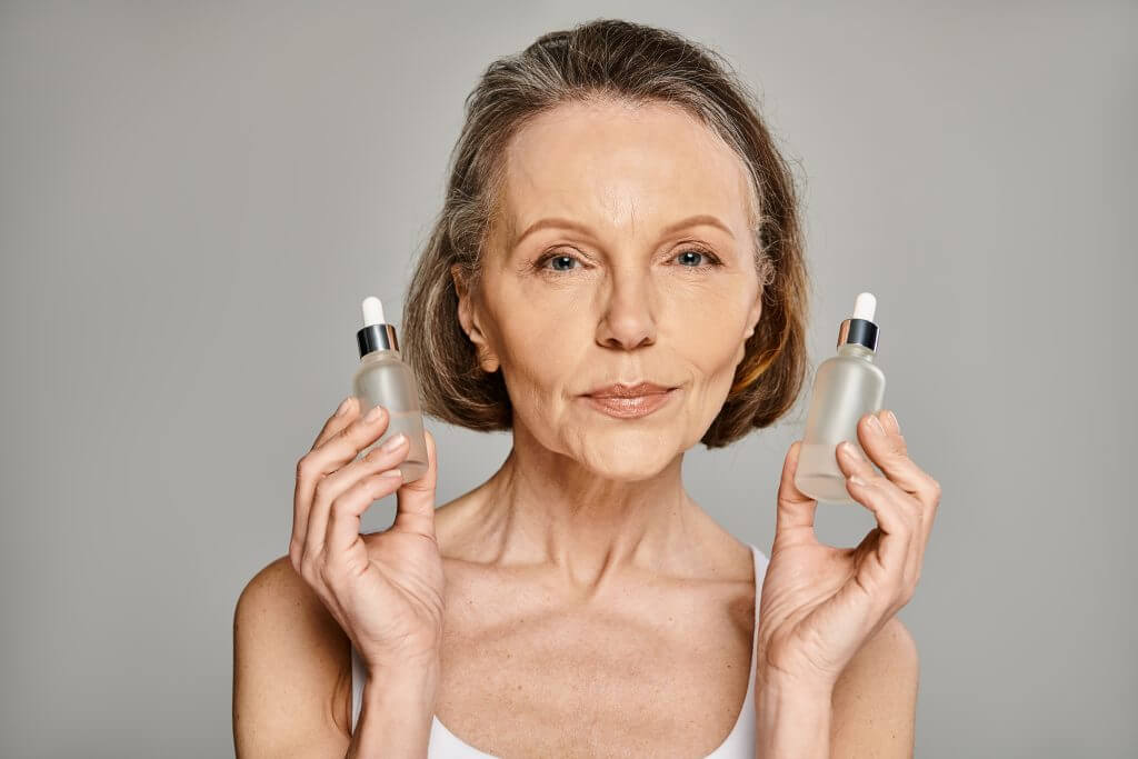 a mature, attractive woman elegantly holds two bottles of skin care products.