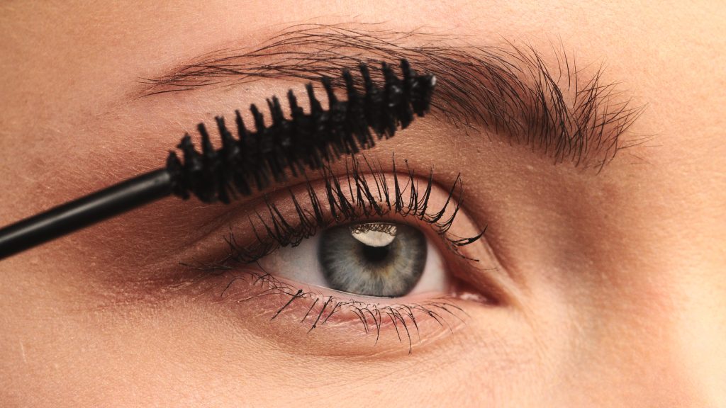 closeup shot, stylist applies black mascara on the eyelashes of